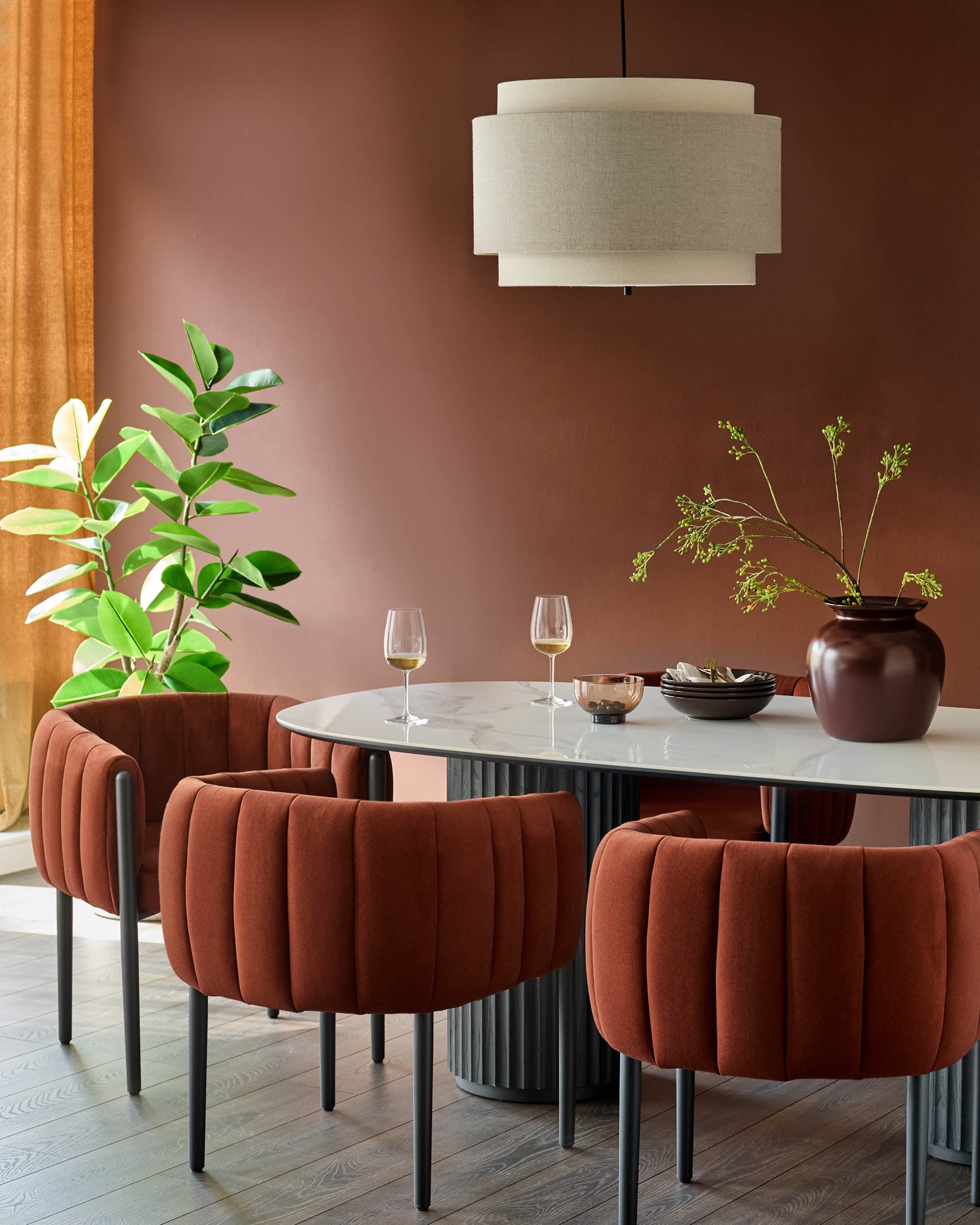Dining area with upholstered chairs, marble table, statement light fixture and house plant in a modern, stylish space.