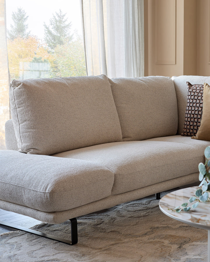 Colette left-hand corner chaise sofa in natural fabric, shown at an angle with decorative pillows, in a bright living room.