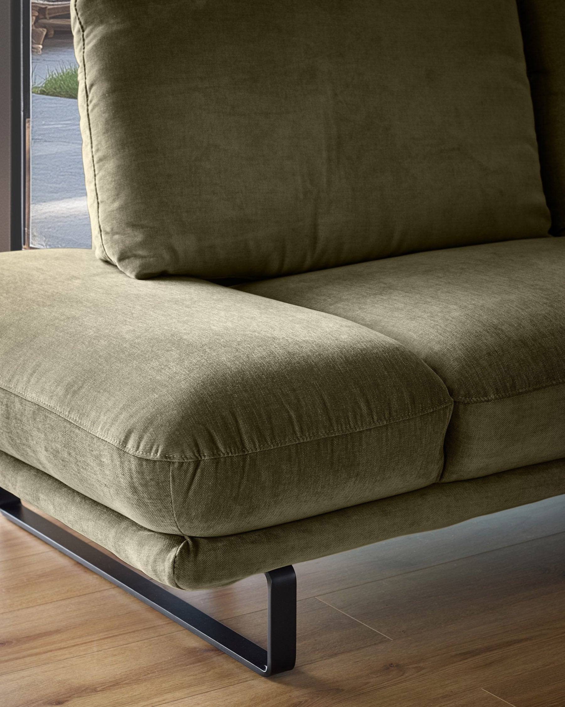 Olive green fabric corner chaise sofa with plush cushions and black metal legs, photographed from a side angle.
