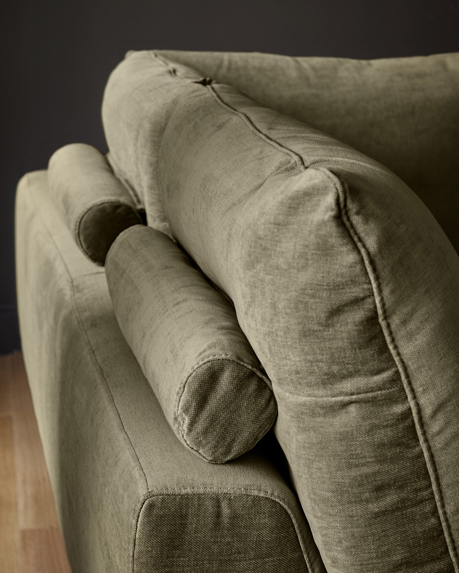 Colette left-hand corner chaise sofa in olive green fabric, shown at an angle highlighting the curved armrest and cylindrical bolster cushion.