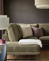Olive green left-hand corner chaise sofa with decorative pillows and cream throw blanket in a styled living room setting.