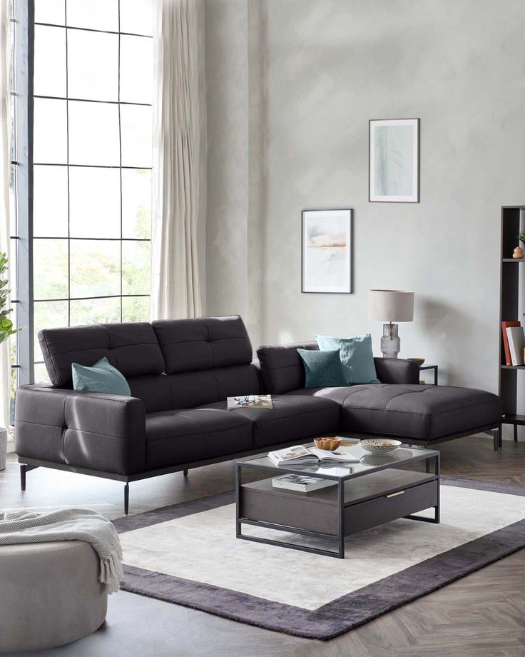 Modern black sectional sofa with teal cushions, glass-top coffee table, decorative items, and a cozy rug in a bright space.