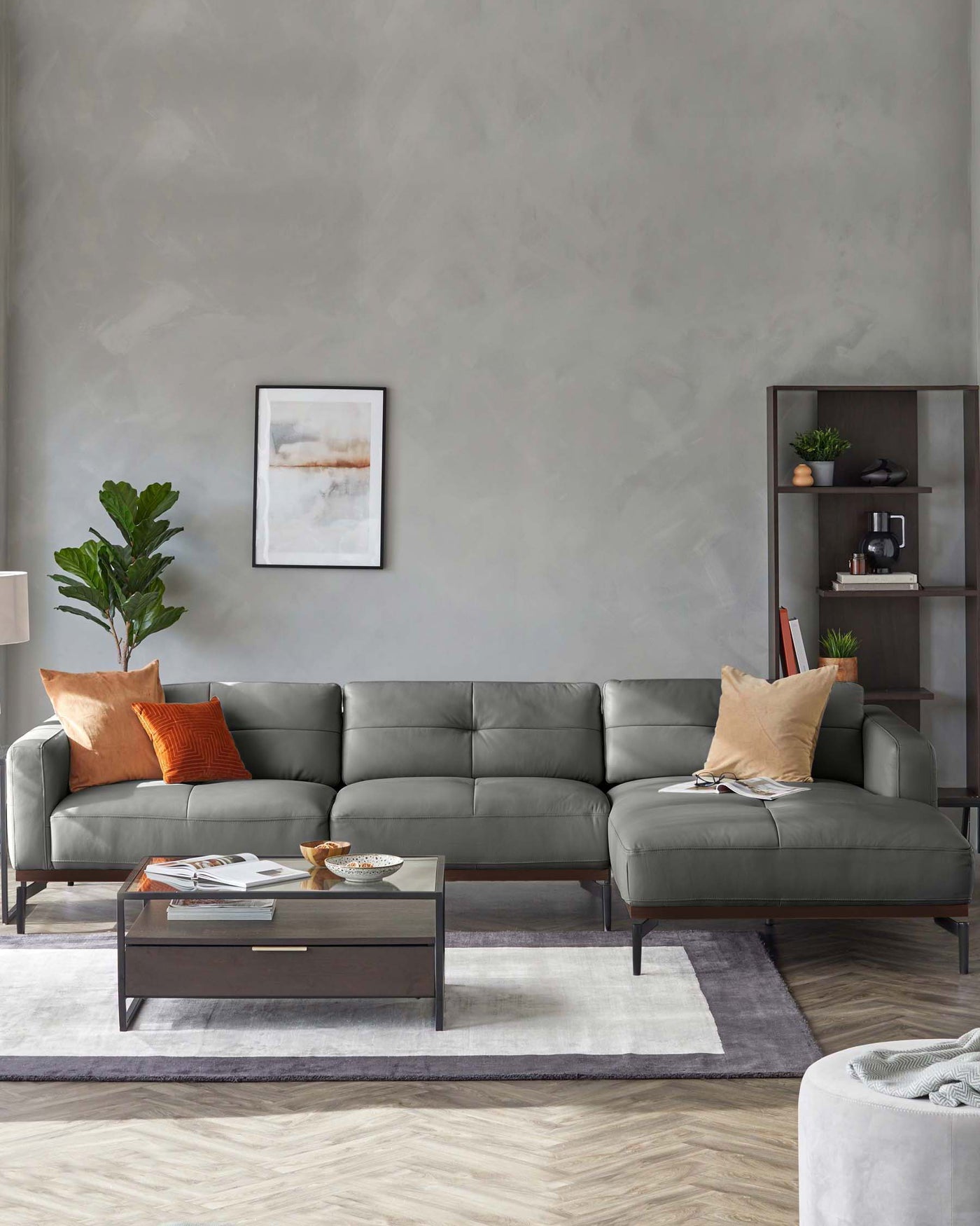 Modern living room setup featuring a grey L-shaped sectional sofa with plush cushions and a sleek dark wooden frame. In front of the sofa is a rectangular wooden coffee table with a dark finish, holding decorative items and books. To the right, a dark wood bookshelf is adorned with a variety of decorative objects and plants, contributing to a contemporary aesthetic.