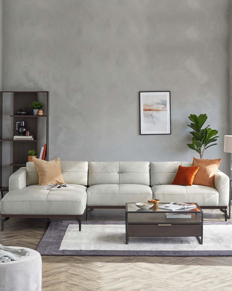 Contemporary light grey sectional sofa with chaise, modern dark wood coffee table with metal accents, and a matching dark wood open shelving unit. The setup is complemented by an off-white and grey area rug, a side lamp with a cylindrical shade, and various decorative pillows in neutral and warm tones.