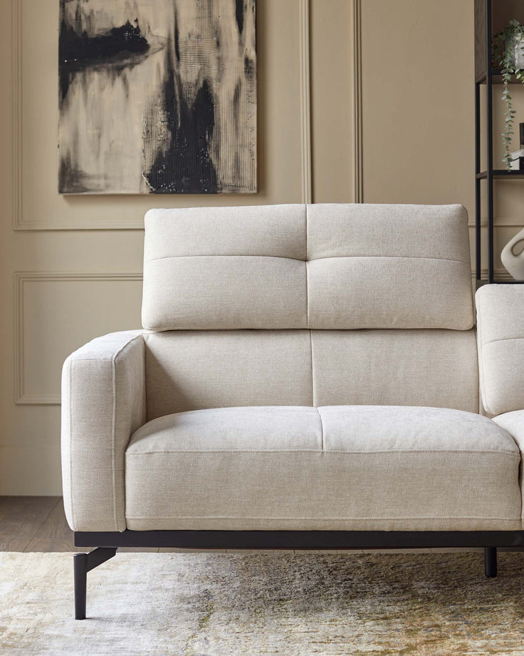 A stylish, light-coloured sofa with a modern black frame, complemented by a textured rug and abstract art.
