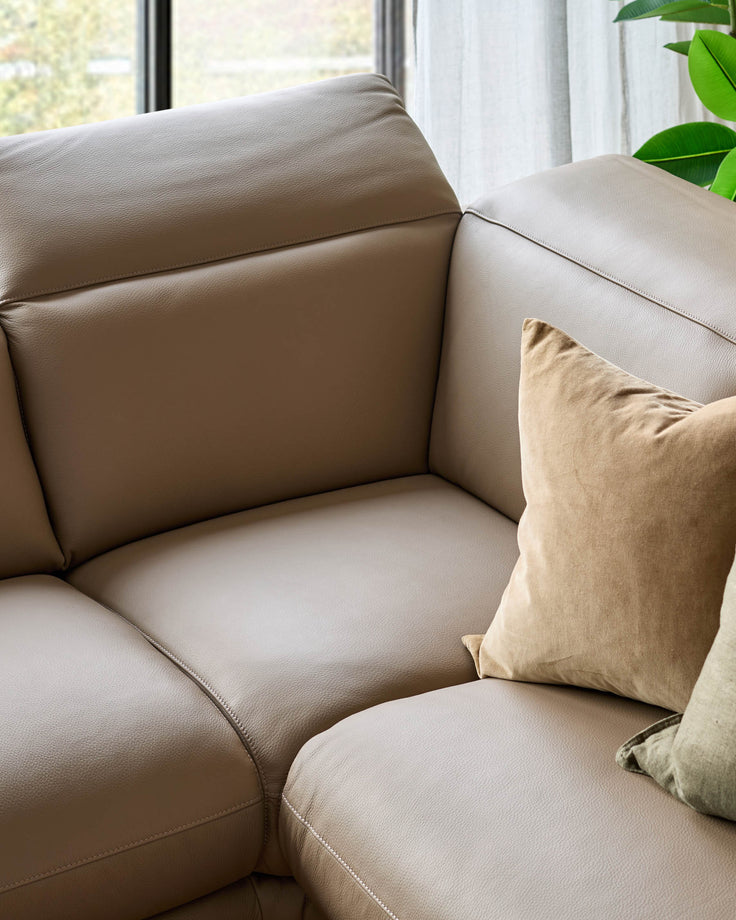 Connor left-hand corner chaise sofa in natural leather with cushioned armrest and beige throw pillow by window.