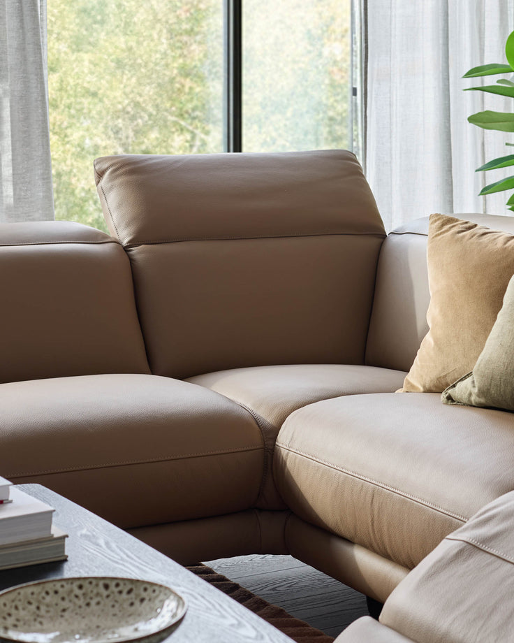 Connor left-hand corner chaise sofa in natural leather, angled view showing curved armrests and plush seating by bright window.