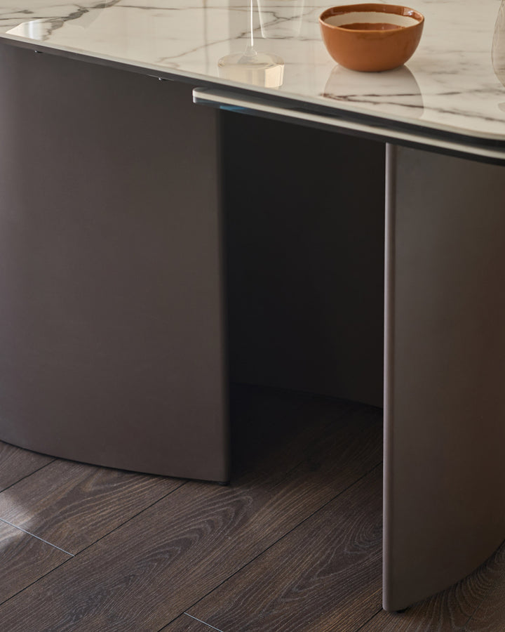 Cortona dining table with marble-effect ceramic top, dark Grey base, and metal handle detail, seated view.