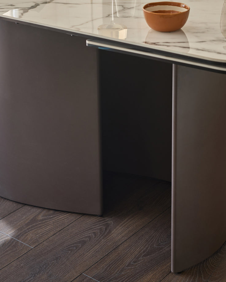 Cortona dining table with marble-effect ceramic top, dark Grey base, and metal handle detail, seated view.