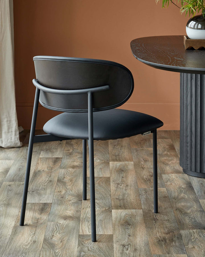 A modern black chair sits next to a round table with fluted pedestal. Simple and elegant design.