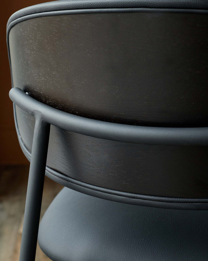 A close up of the back of a black chair with wood and leather-like material.