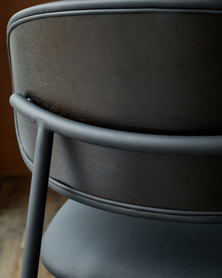 A close up of the back of a black chair with wood and leather-like material.