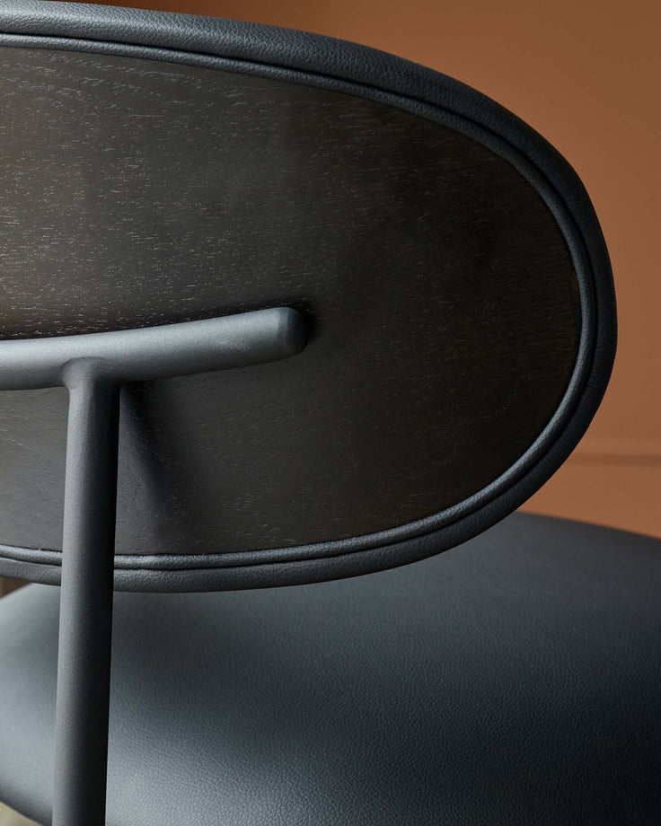 Close-up of a stylish black chair with a rounded back and a textured leather seat, exuding modern sophistication.
