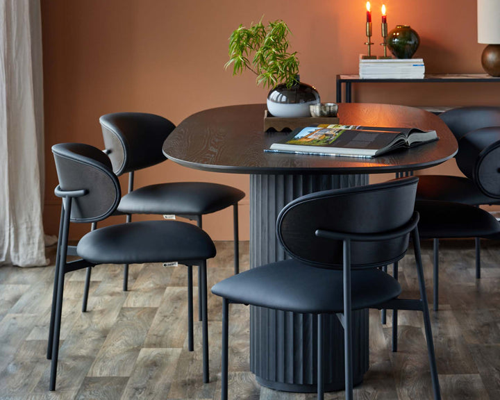 A dining area features a black round table and chairs set against a terracotta wall and timber flooring.