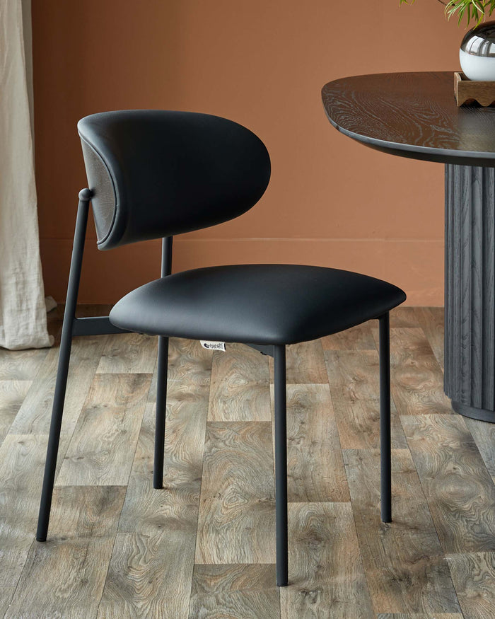 A stylish black chair sits next to a dark wood round table, showcasing modern furniture design.