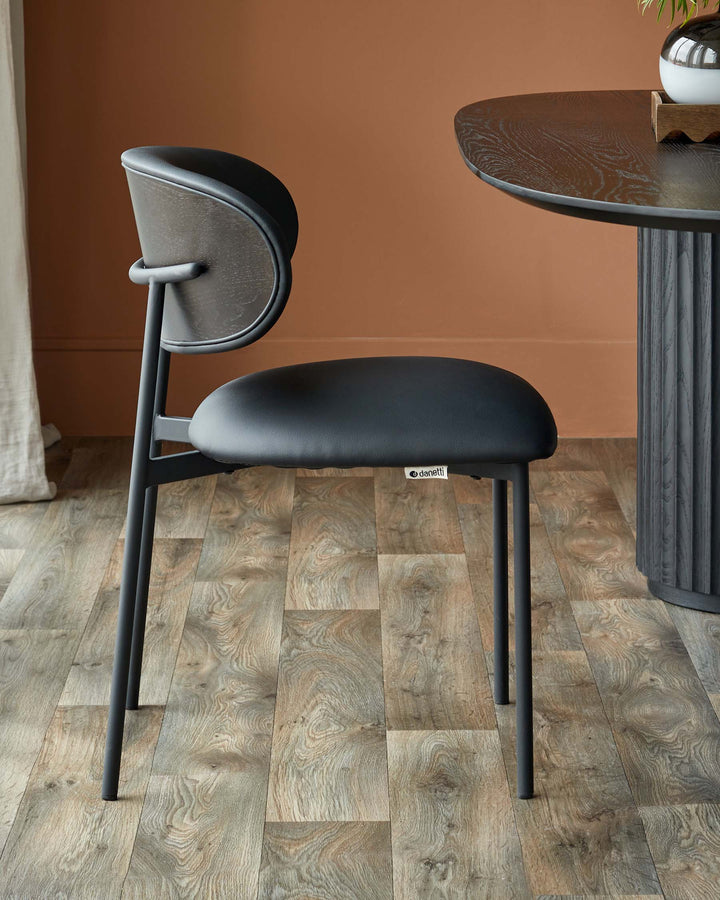 A stylish dark grey dining chair with a curved back, sat next to a round wooden dining table.
