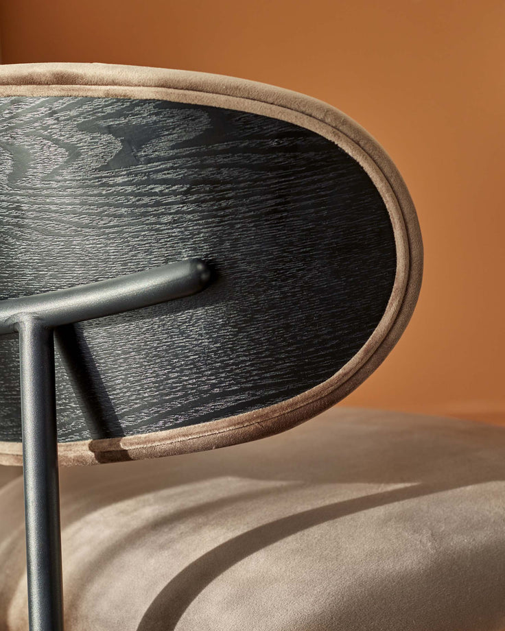 Close up of a stylish chair back with a wooden panel, soft fabric trim, and a sleek, metal frame.