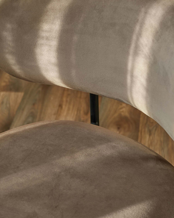 Close-up of two stylish chairs with brown velvet fabric and a black metal support, set against a wood floor.