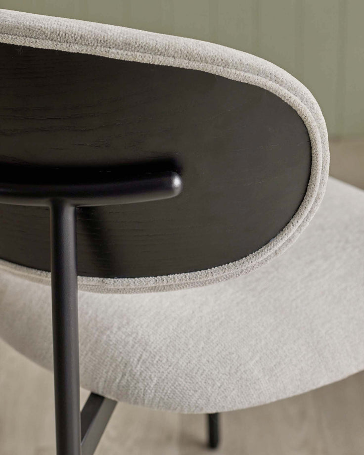 Close up of a grey chair with a curved upholstered back and sleek black frame. Modern design for stylish living spaces.
