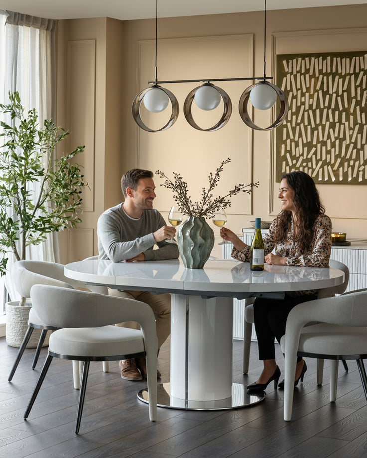Curva white gloss round extending dining table with chrome base, set for two with matching white curved chairs.