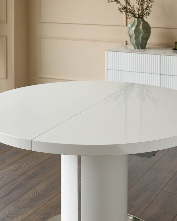 White gloss round extending dining table with cylindrical pedestal base, shown partially extended on wooden flooring.