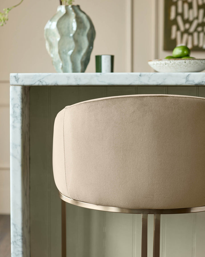 Dakota velvet barstool in champagne with brass base, shown beside marble countertop in modern interior setting.