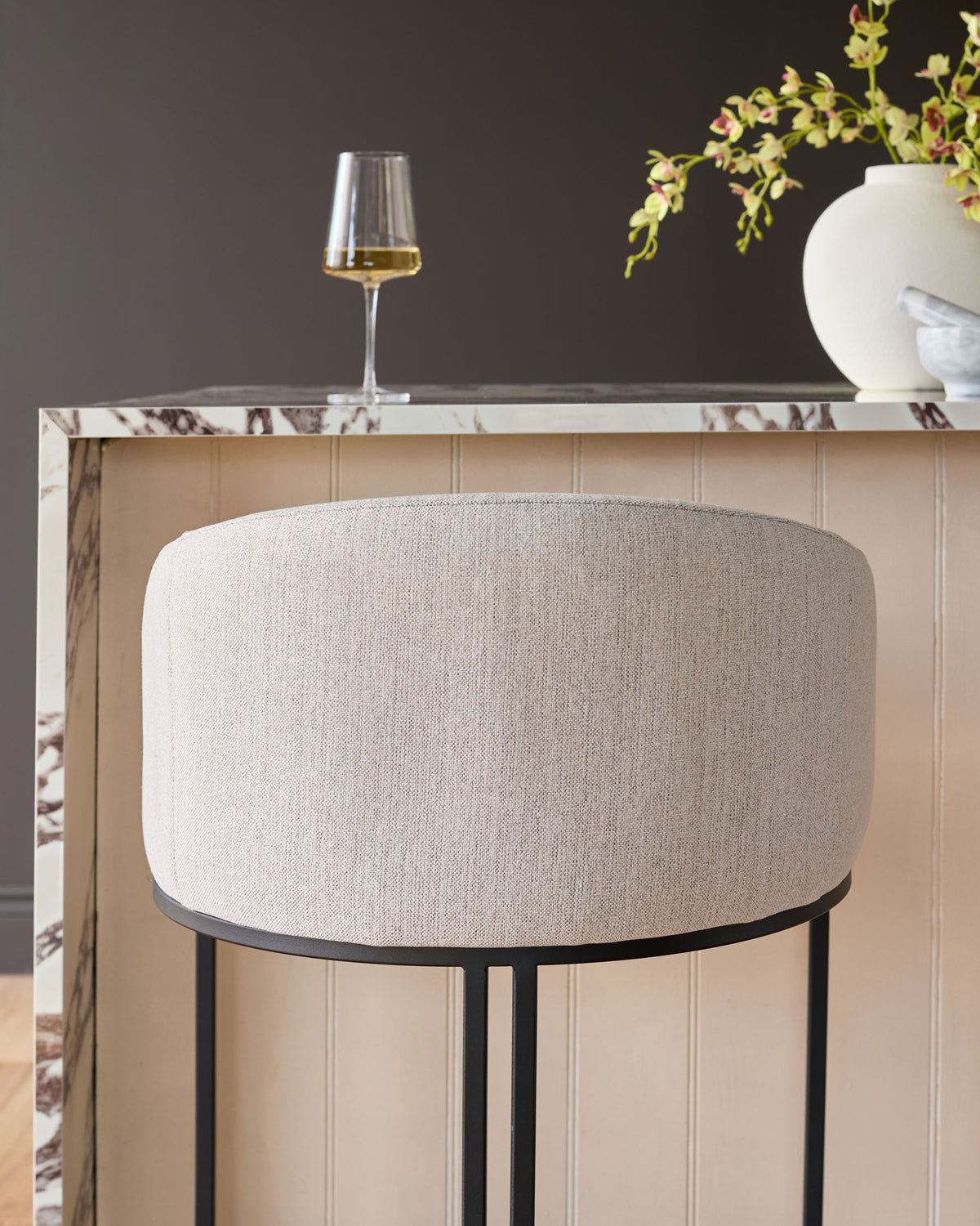 Dakota bar stool in natural fabric with black metal frame, shown against marble countertop in styled interior setting.