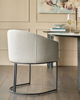 Dakota dining chair in natural fabric with curved back and black metal frame, shown from rear angle at a desk.