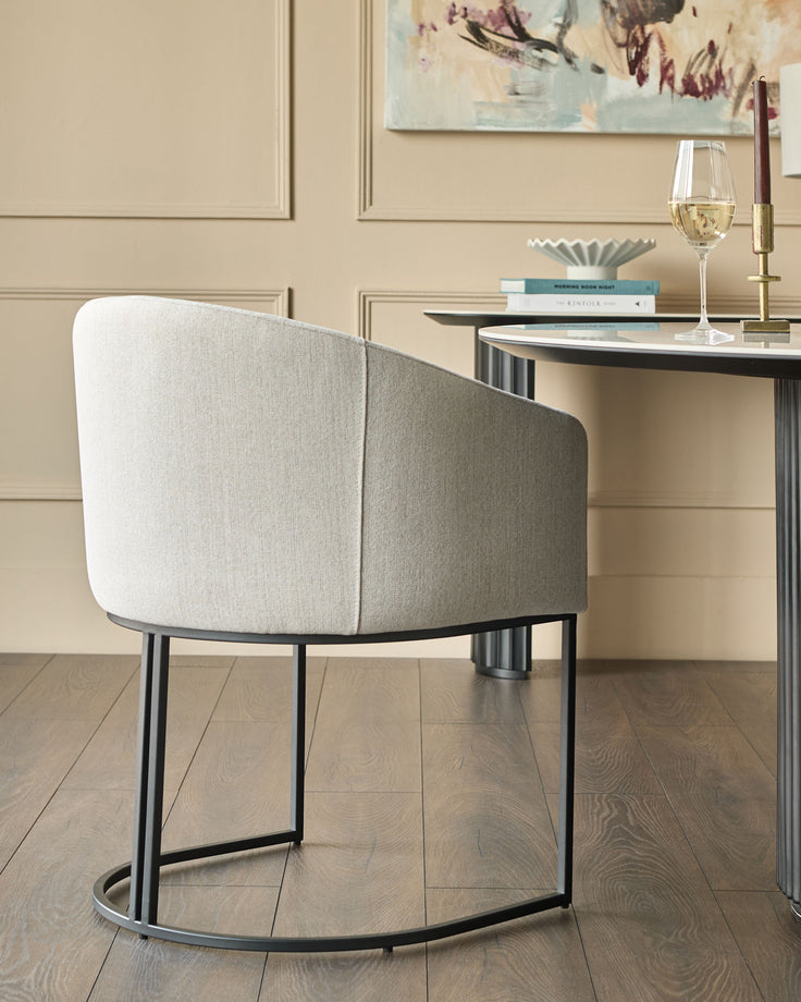 Dakota dining chair in natural fabric with curved back and black metal frame, shown from rear angle at a desk.