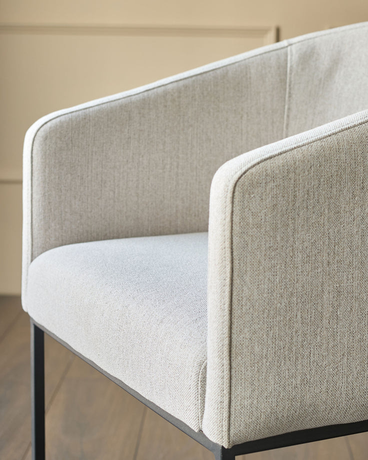 Dakota dining chair in natural fabric, shown from side angle with curved back and armrests on black legs.