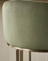 Dakota bar stool in olive green velvet with brushed metal base and footrest detail, close-up side view.
