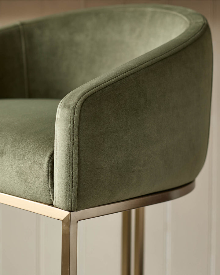 Dakota bar stool in olive green velvet with curved backrest and brass metal frame, side detail view.