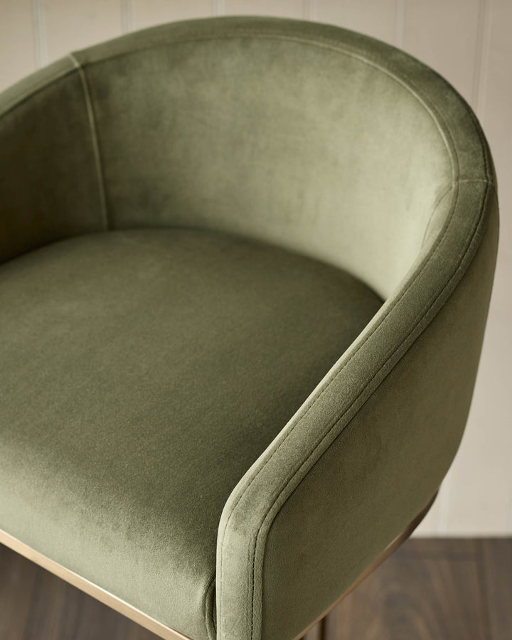 Dakota bar stool in olive green velvet, showing curved backrest and seat from a side angle view.