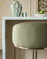 Dakota bar stool in olive green velvet with brushed gold footrest, shown at marble countertop.