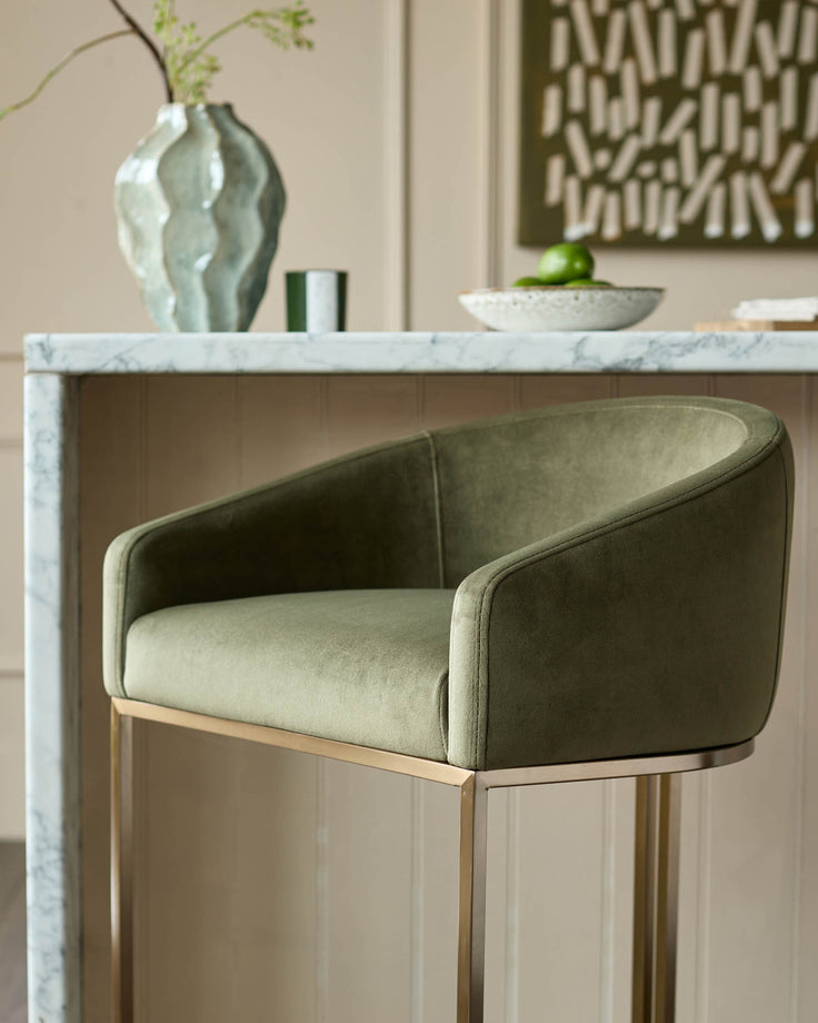 Dakota bar stool in olive green velvet with curved backrest and brushed metal frame, shown at marble countertop.
