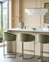Dakota bar stool in olive green velvet with brushed gold metal frame, shown in set of three at marble countertop.