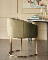 Dakota dining chair in olive green velvet with curved back, brass legs, shown at desk in modern room setting.