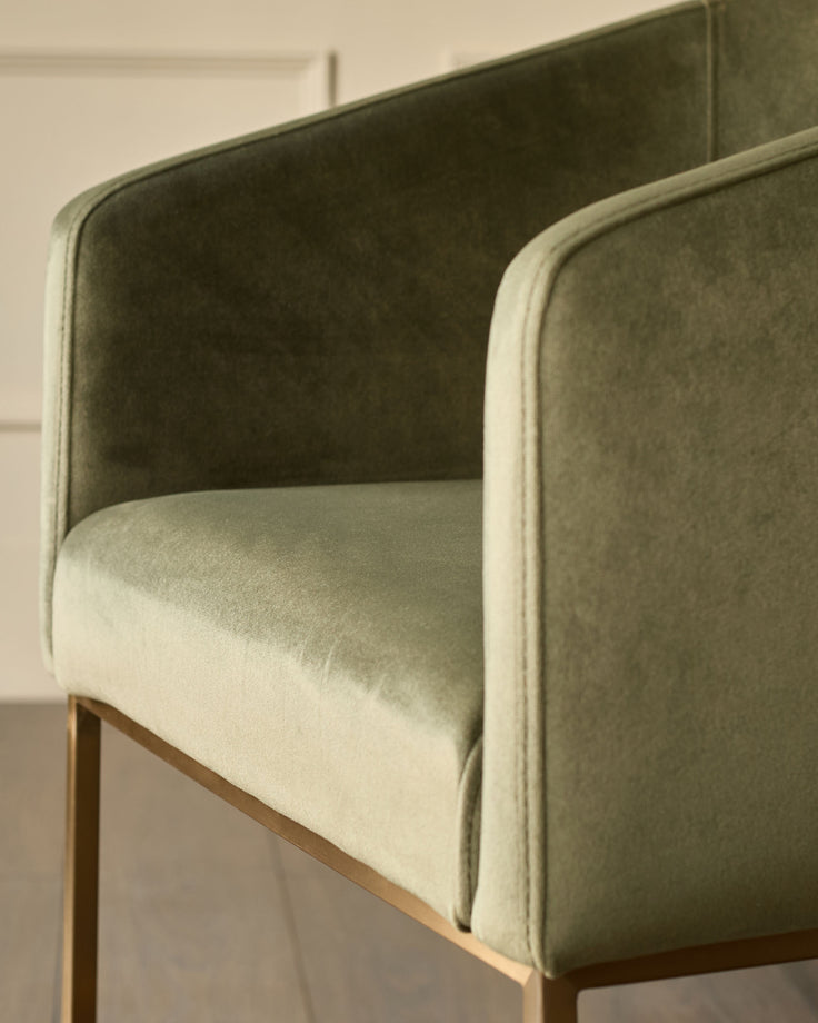 Dakota dining chair in olive green velvet with curved backrest and wooden legs, side view detail.