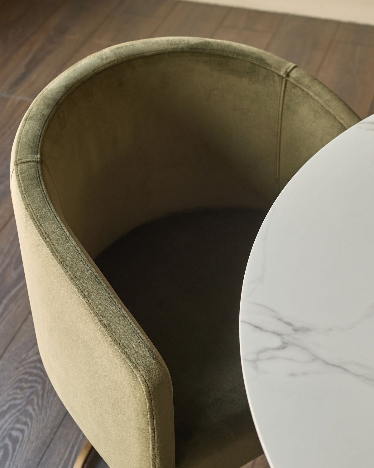 Dakota dining chair in olive green velvet, shown from above at an angle with white marble side table nearby.