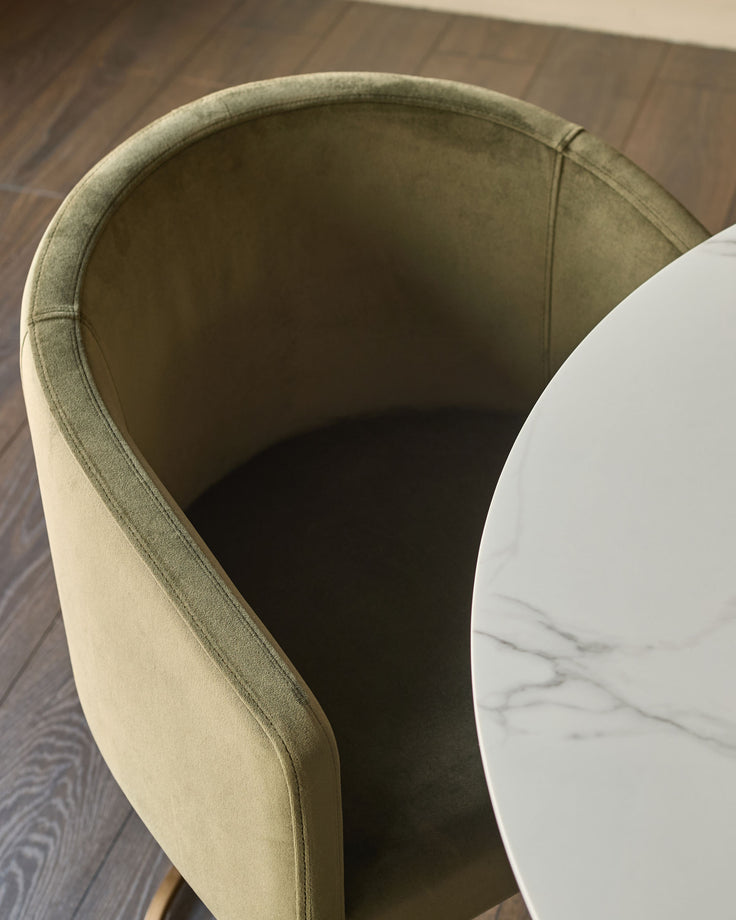 Dakota dining chair in olive green velvet, shown from above at an angle with white marble side table nearby.