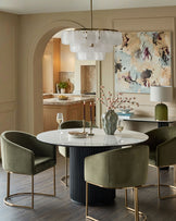 Dakota dining chair in olive green velvet with brass frame, shown around white round table in modern dining room.
