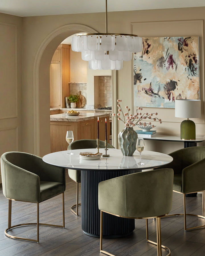 Dakota dining chair in olive green velvet with brass frame, shown around white round table in modern dining room.