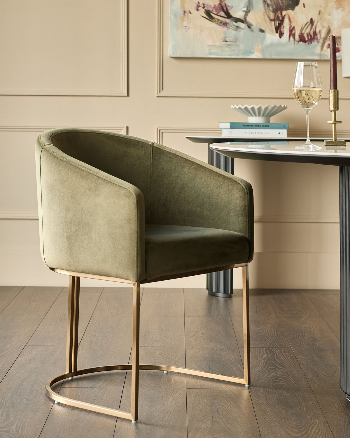 Dakota dining chair in olive green velvet with brass legs, shown in a styled room setting next to a desk.