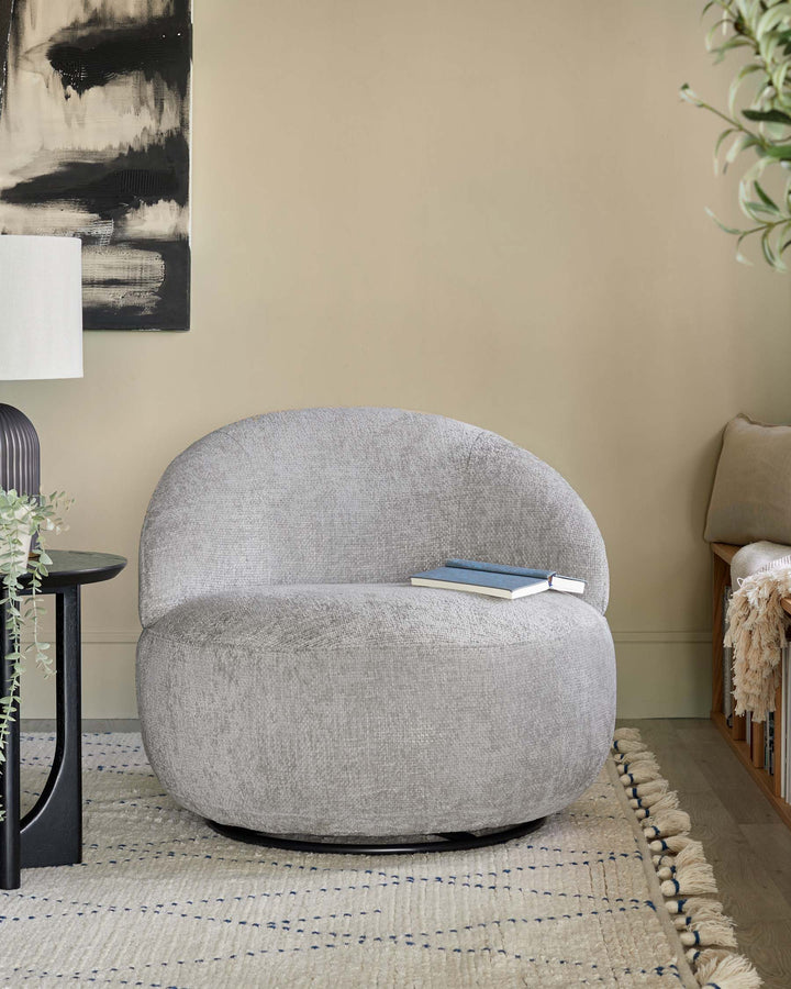 A modern, round gray chair with textured upholstery, paired with a sleek black side table and a decorative lamp.