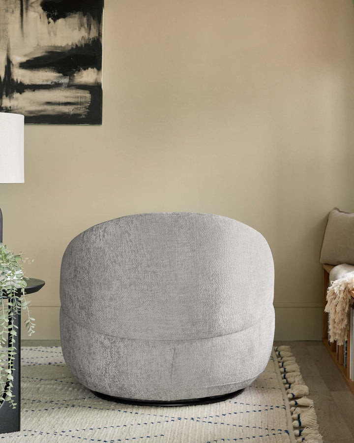 A plush, gray round accent chair with a soft texture, set on a neutral-toned rug, accompanied by a small black table and greenery.