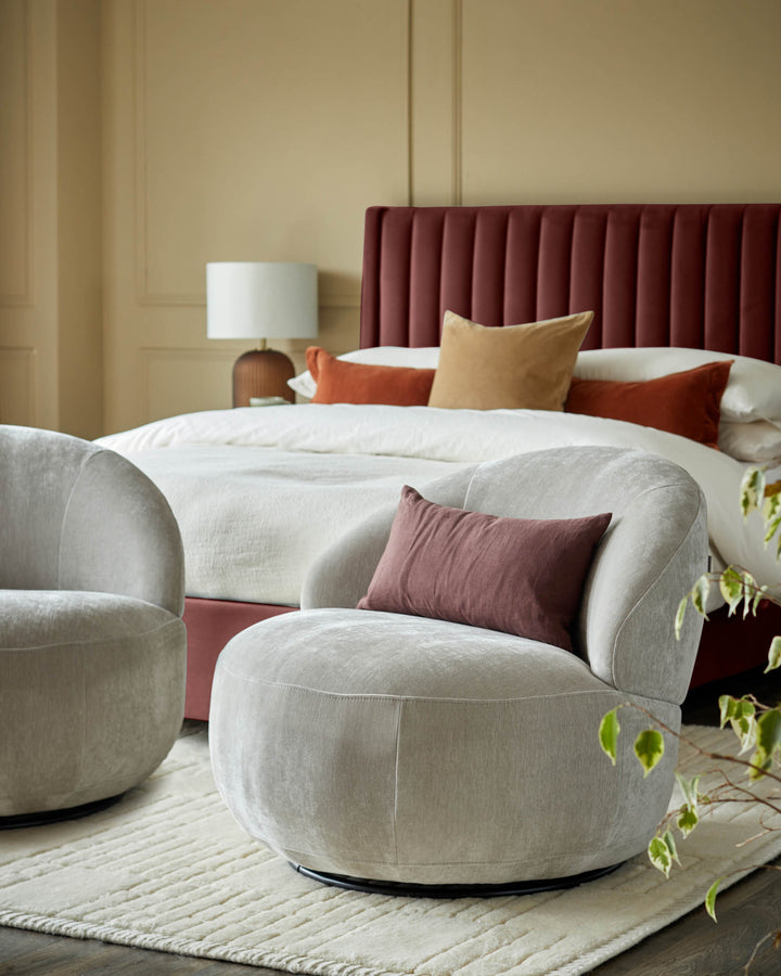 Bedroom scene with two round swivel chairs in neutral tones, facing a double bed with a red headboard.