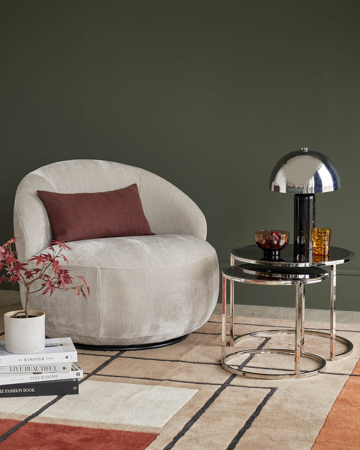 Stylish armchair with a burgundy cushion, next to a nesting table with a chrome lamp, sat on a geometric rug.