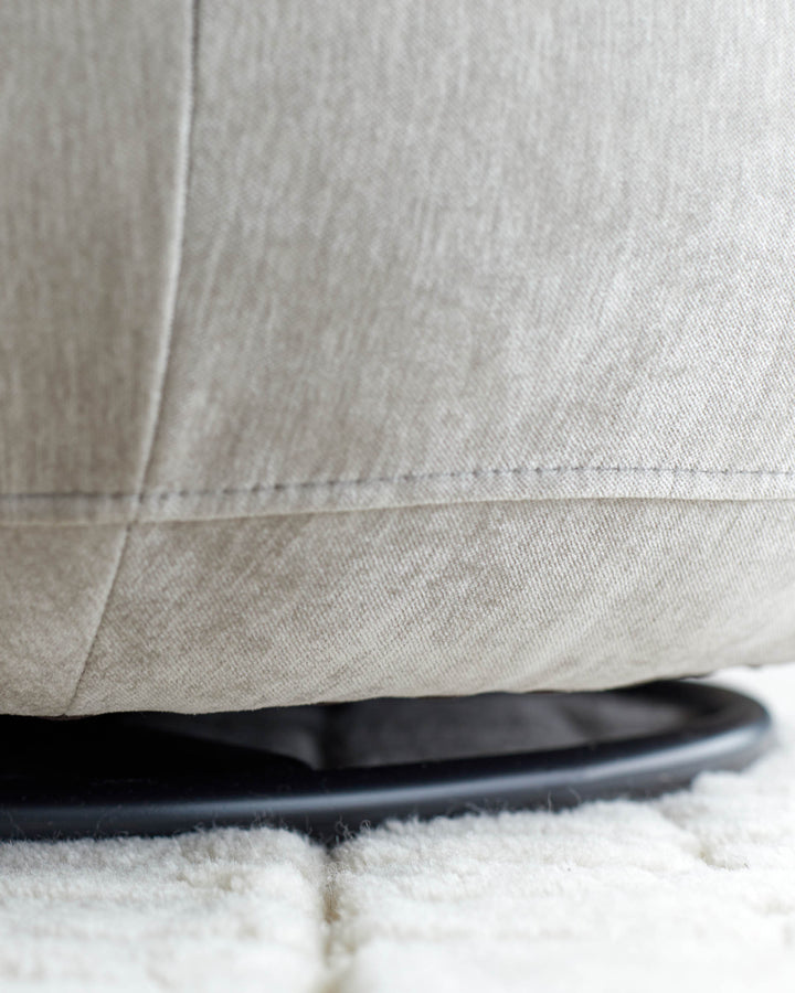 Close-up of a swivel chair's base, showcasing the fabric texture, dark metal ring, and a soft, white rug underneath.