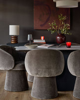 Mocha fabric swivel dining chair with rounded, curved backrest and cylindrical base, shown in a styled dining room setting.