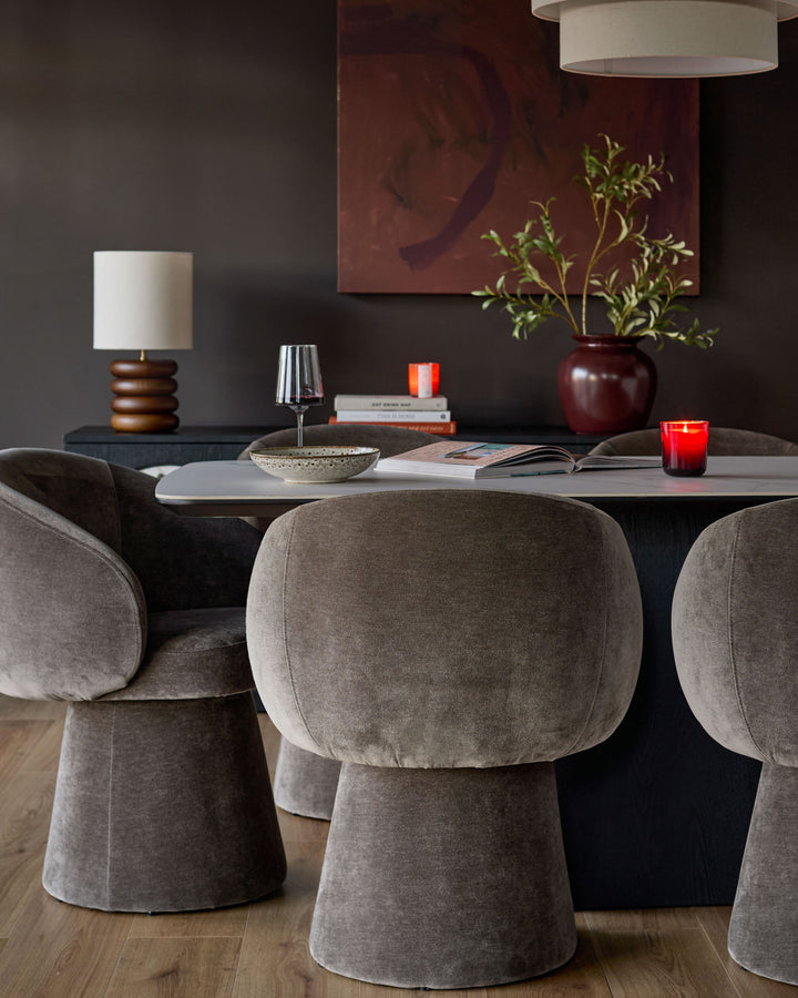 Mocha fabric swivel dining chair with rounded, curved backrest and cylindrical base, shown in a styled dining room setting.